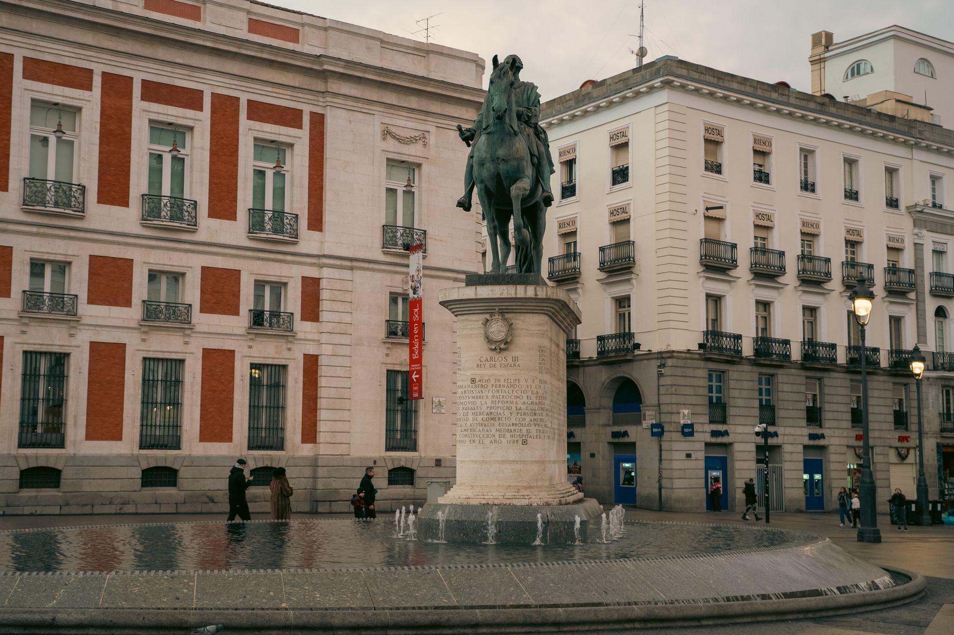 Equestrian statue in vibrant Madrid plaza with classic architecture and people.