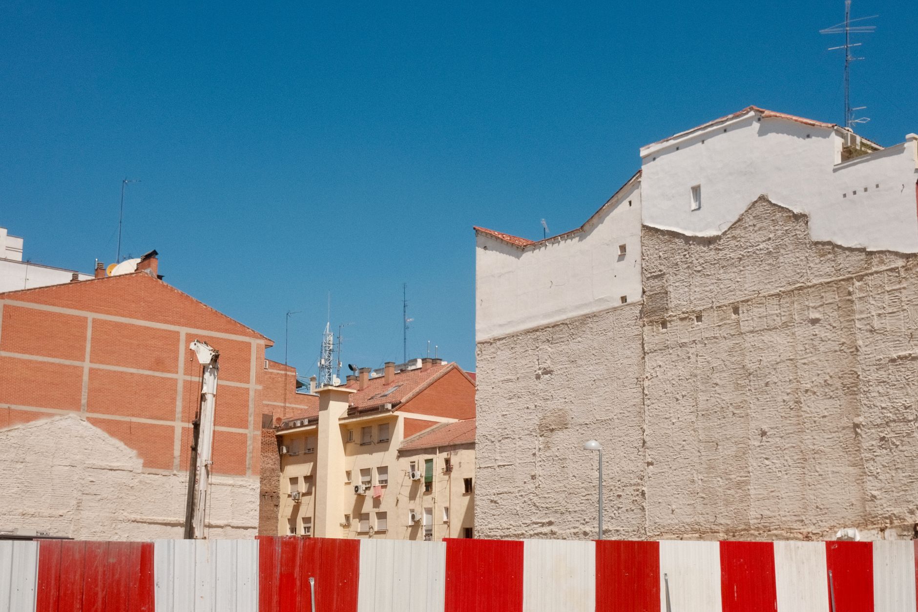Red and white barrier with urban buildings under clear blue sky in Madrid. — illustrating How Does Madrid Handle Summer Heat, Practically?