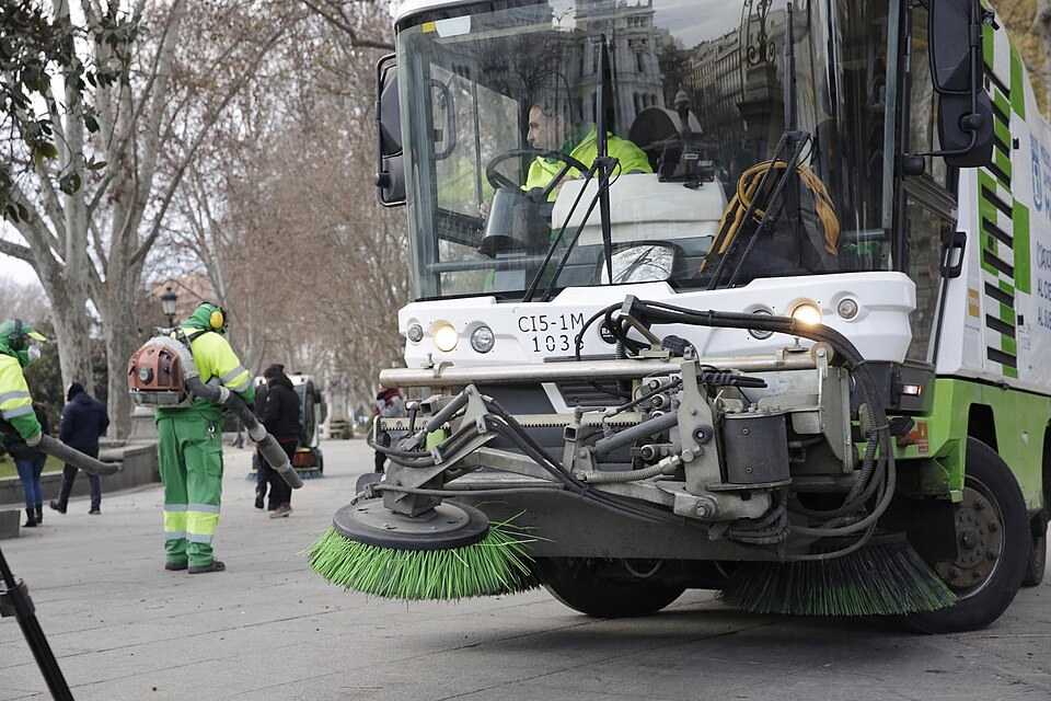 A street-sweeping machine and cleaning crew working a Madrid street