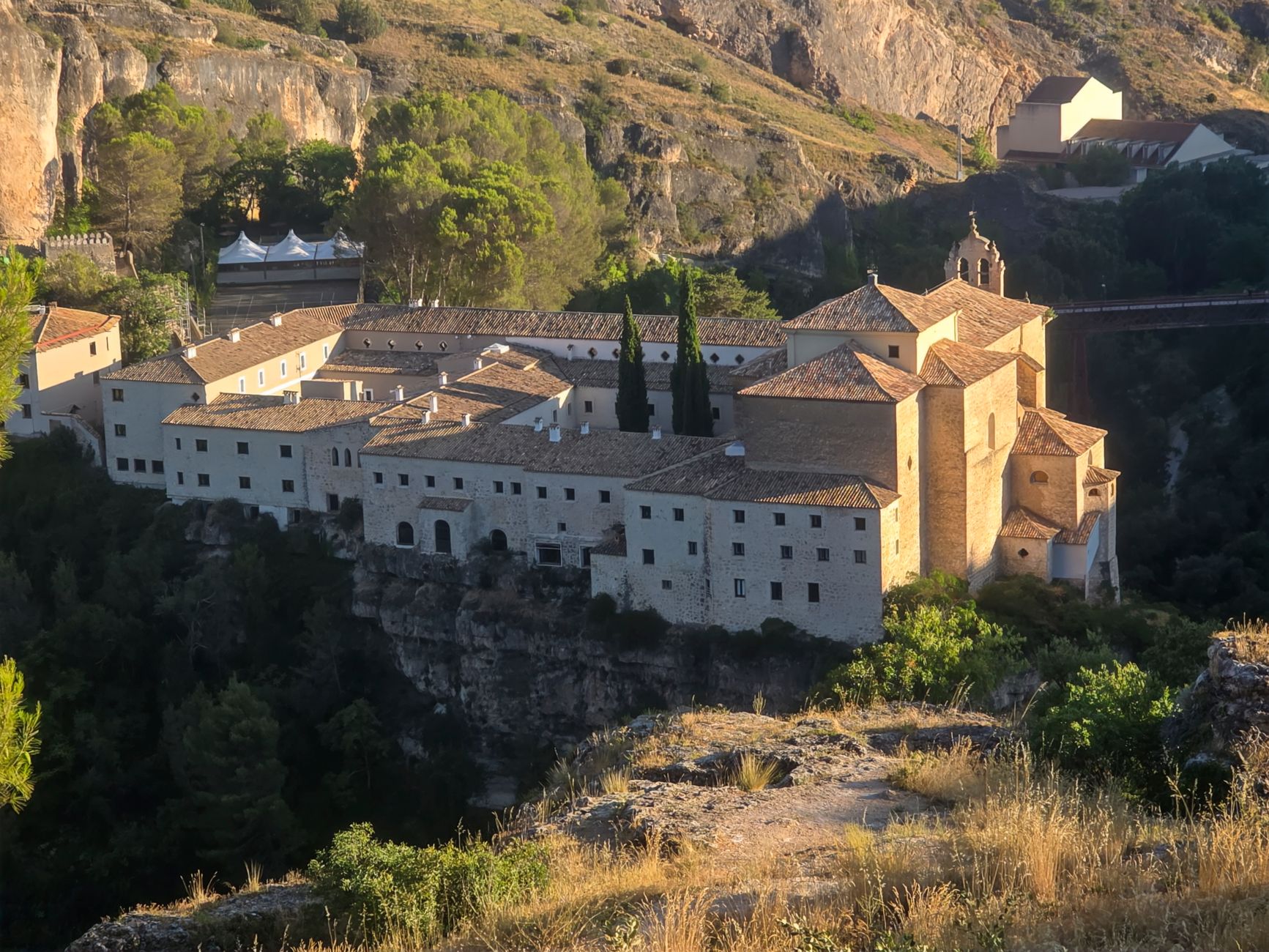 Aerial view of a historic monastery in Cuenca, Spain during daytime, surrounded by cliffs and greenery
