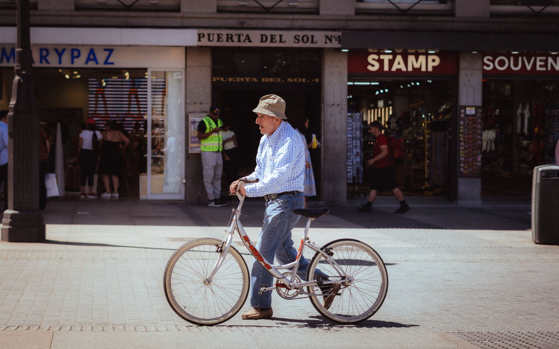 A man walks beside his bicycle in front of shops at Puerta del Sol, Madrid, Spain. — illustrating What Is Madrid’s Low-Emission Zone, and Who Does It Affect?