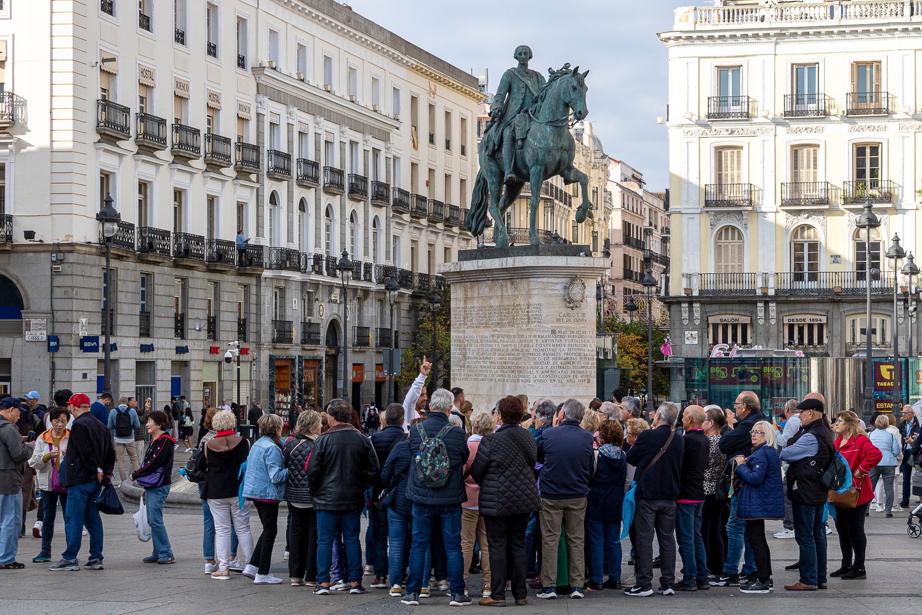 Tourists gather around the equestrian statue in Madrid's Puerta del Sol. Vibrant urban scene.