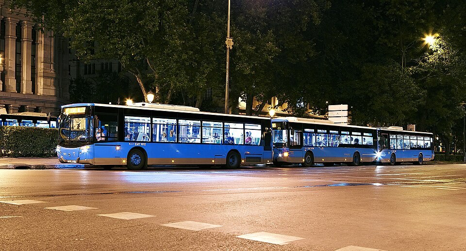 A blue EMT city bus on a Madrid street at dusk