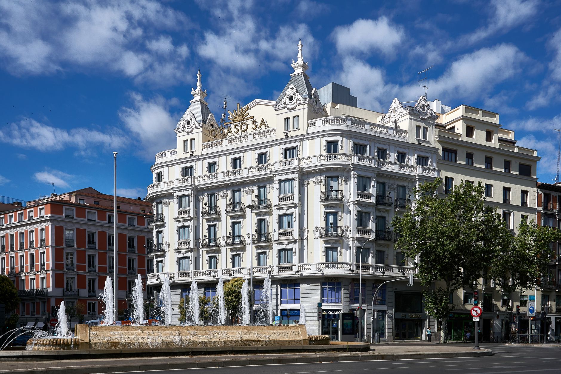 Charming architecture of a classic Madrid building with ornate facade and a lively fountain in daylight.