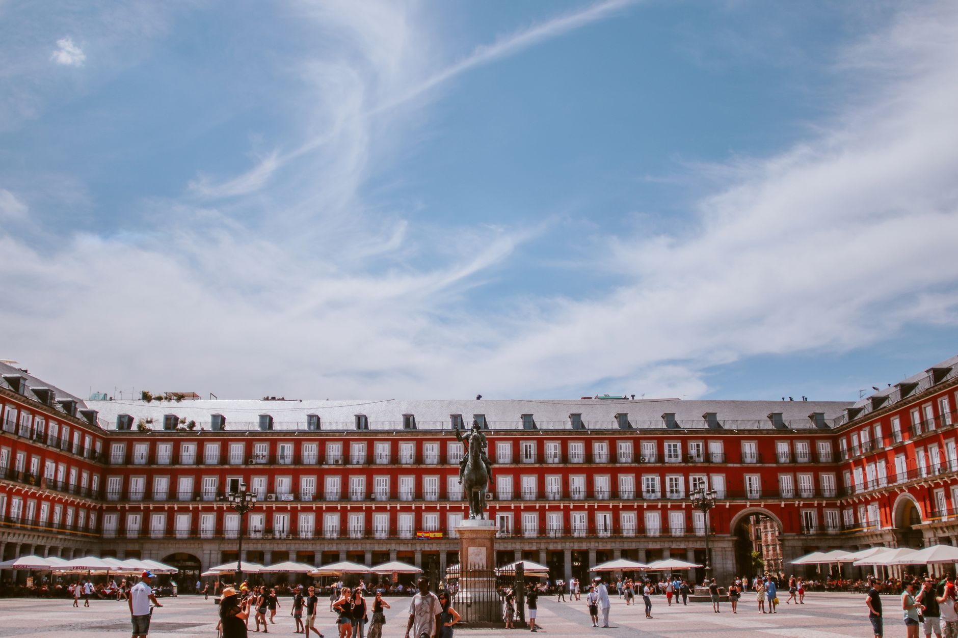 Scenic view of Plaza Mayor in Madrid with a vibrant blue sky and tourists.