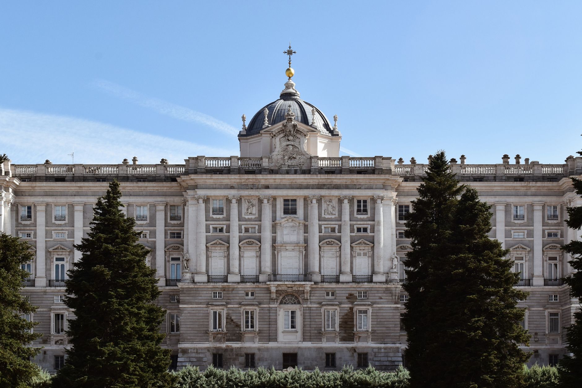 The grand facade of the Royal Palace of Madrid under a clear blue sky, framed by lush trees. — illustrating What Is the Royal Palace of Madrid, and What Can You See?