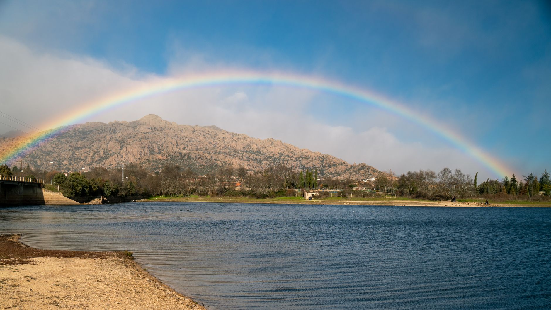 Stunning view of a rainbow arching over the lake and mountains in Manzanares el Real